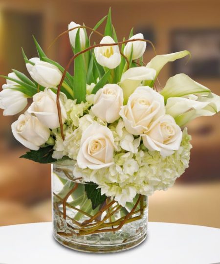 This elegant all-white design is a perfect fit for any occasion. Featuring white roses, miniature calla lilies, white tulips and hydrangeas in a round cylinder vase with curly willow tips, this magnificent bouquet will stand out with an added touch of sophistication and luxury to any home or office.