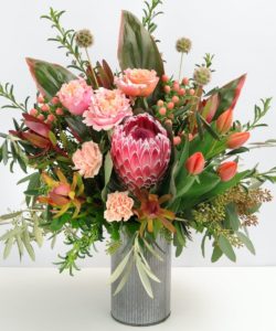 Amongst the Wildflowers is a beautiful arrangement with lush foliage and florals. It's designed in a keepsake rustic tin using flowers such as Protea, Tulips, Carnations, Hypericum Berries & Roses